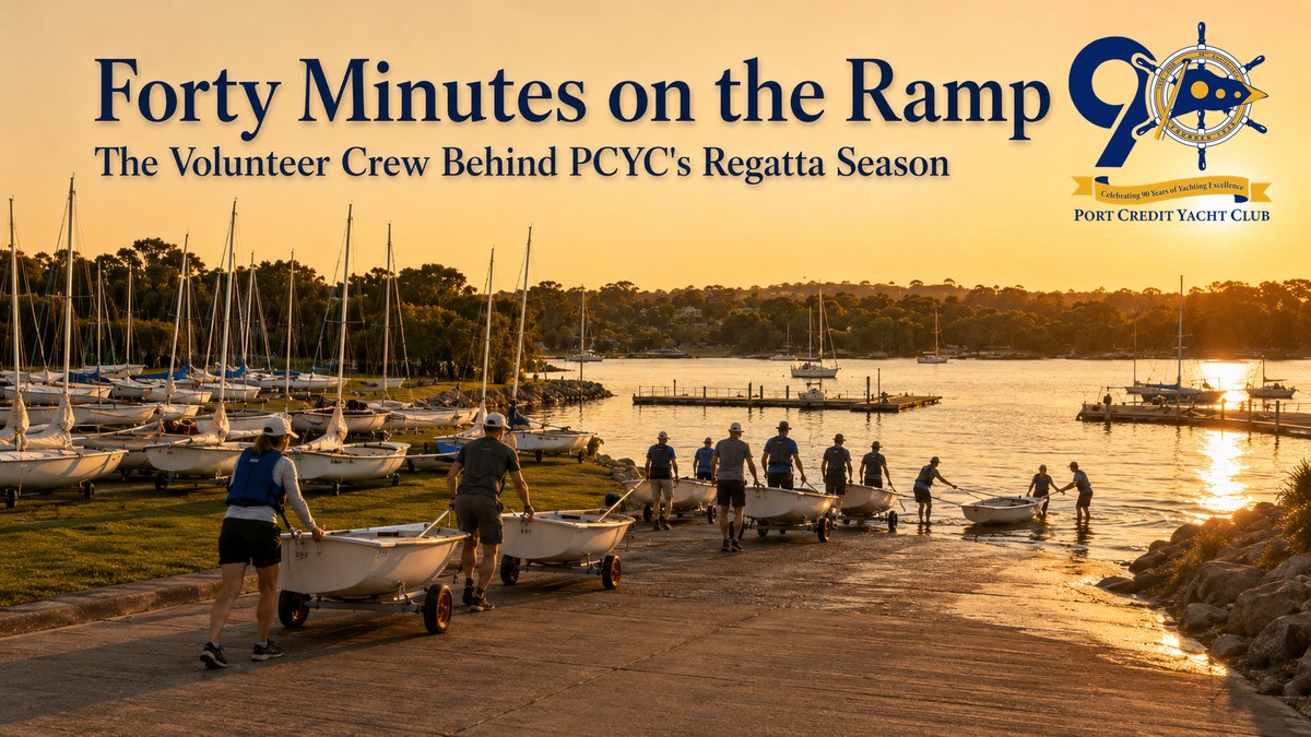 Volunteers at Port Credit Yacht Club moving two-person sailing dinghies on dollies down the launch ramp toward Lake Ontario at sunset, with a boat being floated off its dolly at the waterline.